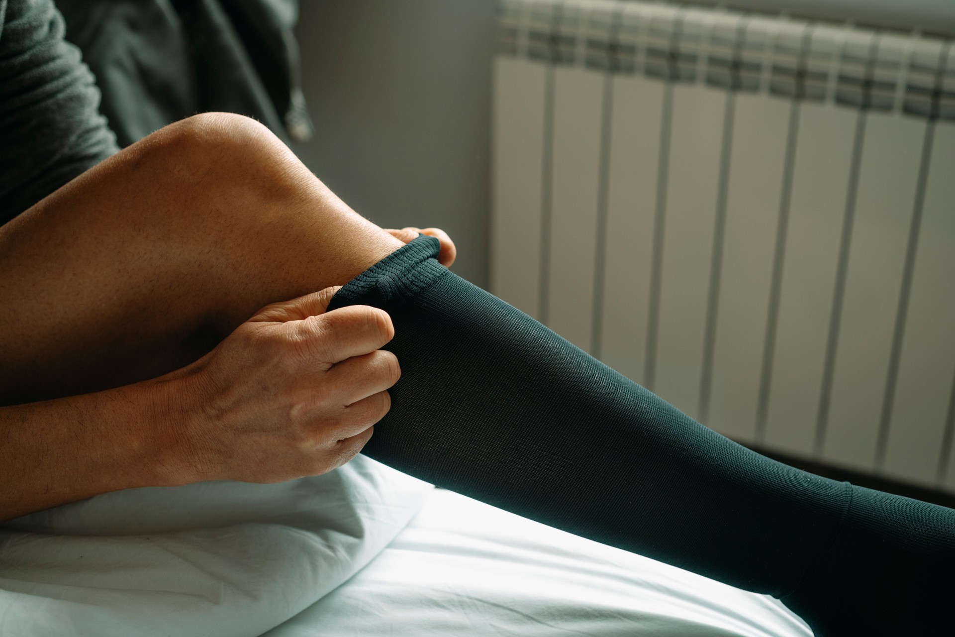 man putting on a compression sock sitting on the bed